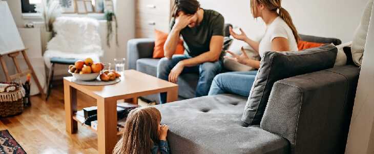 couple arguing on a couch about child support with their child looking at them
