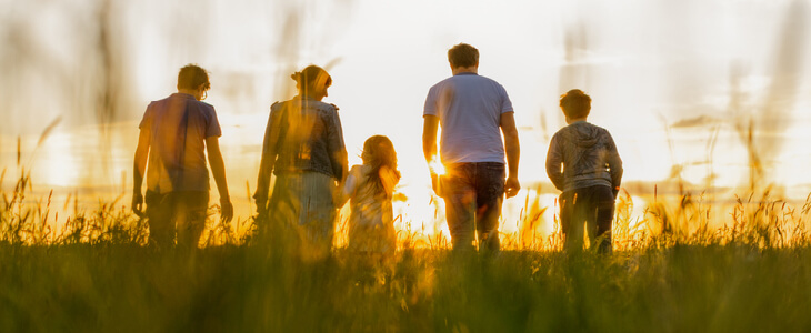 family of five walking in a field during the sunset